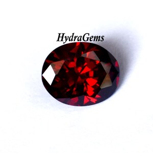 K&ouml;nnte beinhalten: Ein facettierter, oval geformter, tiefroter Edelstein. Der Edelstein hat einen Brillantschliff, der das Licht mit mehreren Facetten reflektiert. Der Text "HydraGems" ist im Bild enthalten.