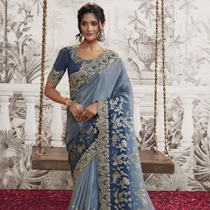 May include: A light blue and dark blue saree with silver embroidery. The saree features a floral pattern and a scalloped border.