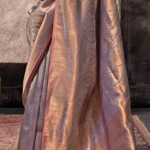 May include: A light purple and gold saree with a paisley pattern. The saree has a pink border.