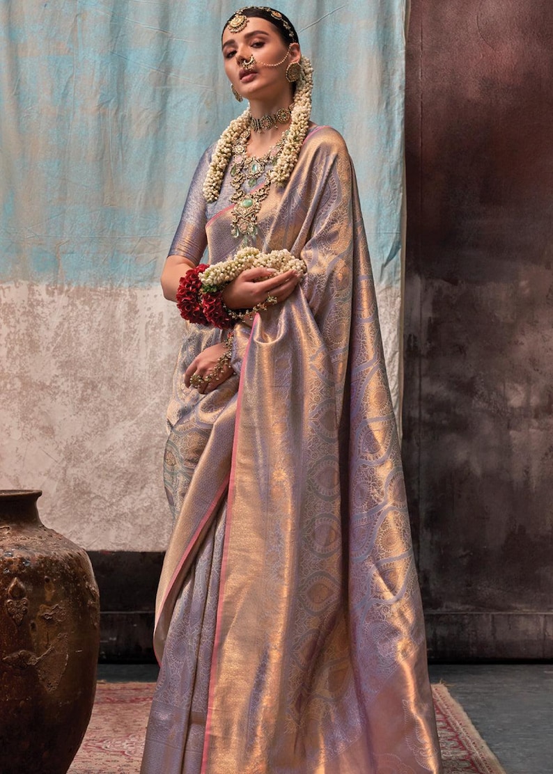May include: A woman wearing a silver and gold saree with a pink border. She is wearing a floral garland and traditional jewelry.