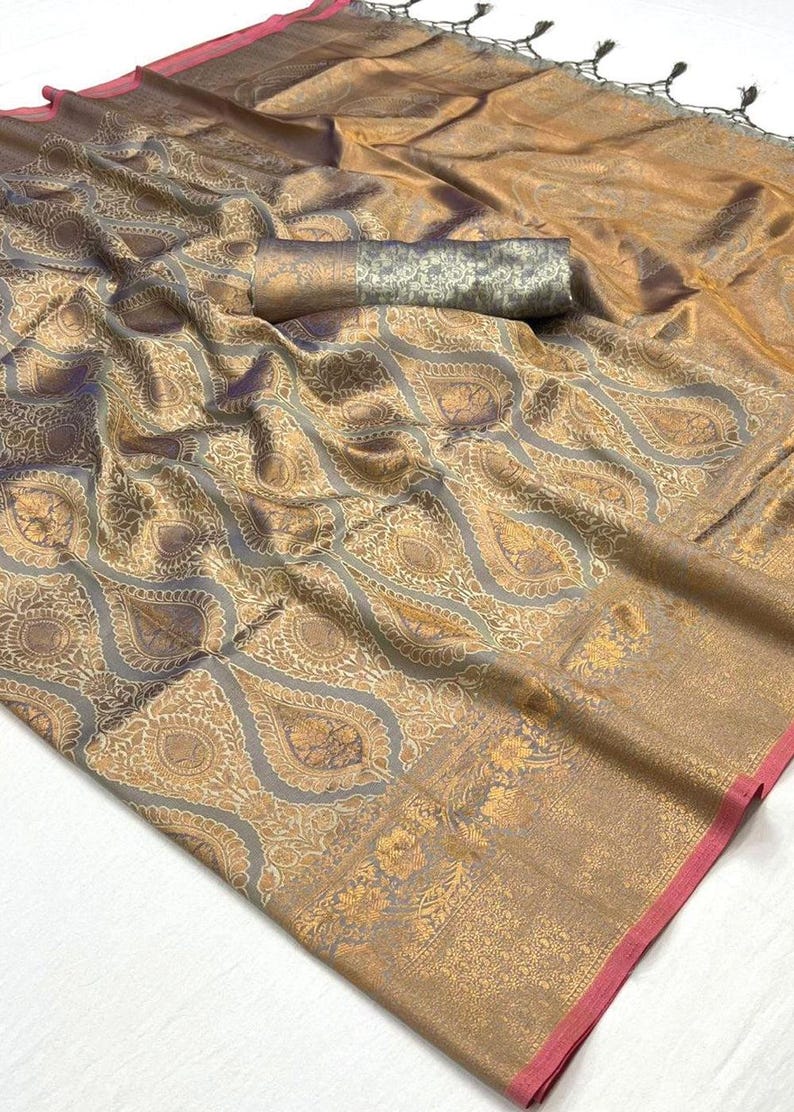 May include: A gold and grey silk saree with a traditional paisley pattern. The saree has a pink border and a silver and gold pallu.