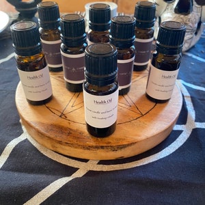 May include: A collection of small, brown glass bottles with black caps, labeled "Health Oil." The bottles are arranged on a round, wooden stand with a pentagram design. The background includes a skull and a black and white patterned cloth.