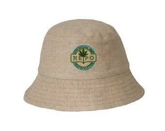 Może przedstawiać: Beżowy kapelusz typu bucket z haftowanym zielonym logo liścia marihuany, na którym w niebieskim kółku widnieje napis "HEMP".