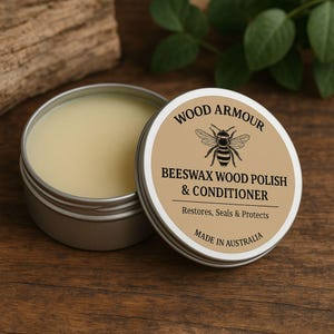 May include: Open tin of beeswax wood polish and conditioner. The label reads "Wood Armour Beeswax Wood Polish & Conditioner" with a bee illustration. The product is made in Australia and is designed to restore, seal, and protect wood surfaces.