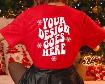 Könnte beinhalten: Ein leuchtend rotes Kurzarm-T-Shirt mit dem weißen Schriftzug "YOUR DESIGN GOES HERE" in einer fetten, geschwungenen Schriftart. Das Design wird durch mehrere weiße Schneeflocken-Illustrationen unterschiedlicher Größe ergänzt.