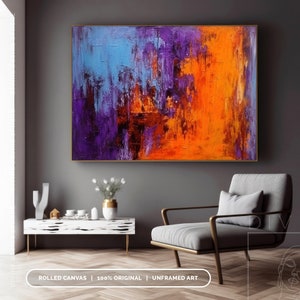 Puede incluir: Pintura abstracta con marco dorado. La obra presenta una superficie texturizada con trazos audaces en azul, morado y naranja. La pintura se exhibe en una pared gris sobre un mueble blanco y un sill&oacute;n gris. El texto en la parte inferior dice: ROLLED CANVAS | 100% ORIGINAL | UNFRAMED ART.
