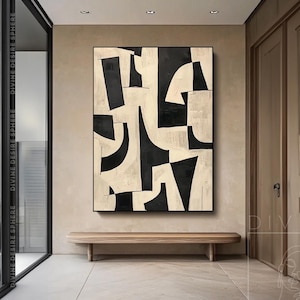 Könnte beinhalten: Abstrakte Schwarz-Weiß-Malerei in einem schwarzen Rahmen. Das Kunstwerk zeigt kräftige, geometrische Formen in kontrastierenden Farben, die eine moderne und auffällige Optik erzeugen. Das Gemälde wird in einem Flur mit einer Holzbank darunter ausgestellt.