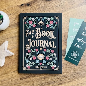 May include: A dark green hardback journal, titled "The Book Journal", with floral decorations in pink, blue, and white. Includes two bookmarks with text. The journal is designed for 100 book reviews.