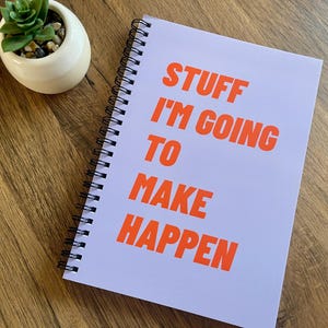 May include: A purple spiral bound notebook with the text "STUFF I'M GOING TO MAKE HAPPEN" in orange.