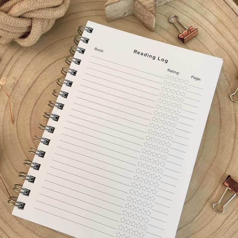 Puede incluir: Un cuaderno Reading Log con espiral, con p&aacute;ginas rayadas y una secci&oacute;n para calificar libros con estrellas. El cuaderno est&aacute; abierto, mostrando el t&iacute;tulo y las indicaciones para registrar los detalles del libro. Sobre una superficie de madera.