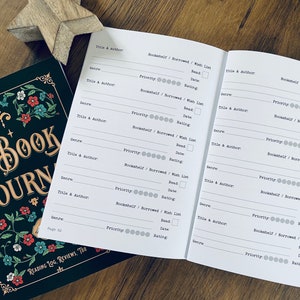K&ouml;nnte beinhalten: Ein schwarzes und gr&uuml;nes Buch mit dem Titel "The Book Journal" auf dem Cover. Das Buch ist auf einer Seite mit einem Lesetagebuch ge&ouml;ffnet, in dem du die B&uuml;cher, die du gelesen hast, verfolgen kannst, einschlie&szlig;lich Titel, Autor, Genre, Priorit&auml;t, B&uuml;cherregal, Leihstatus, Wunschliste, Lesestatus, Datum des Lesens und Bewertung.