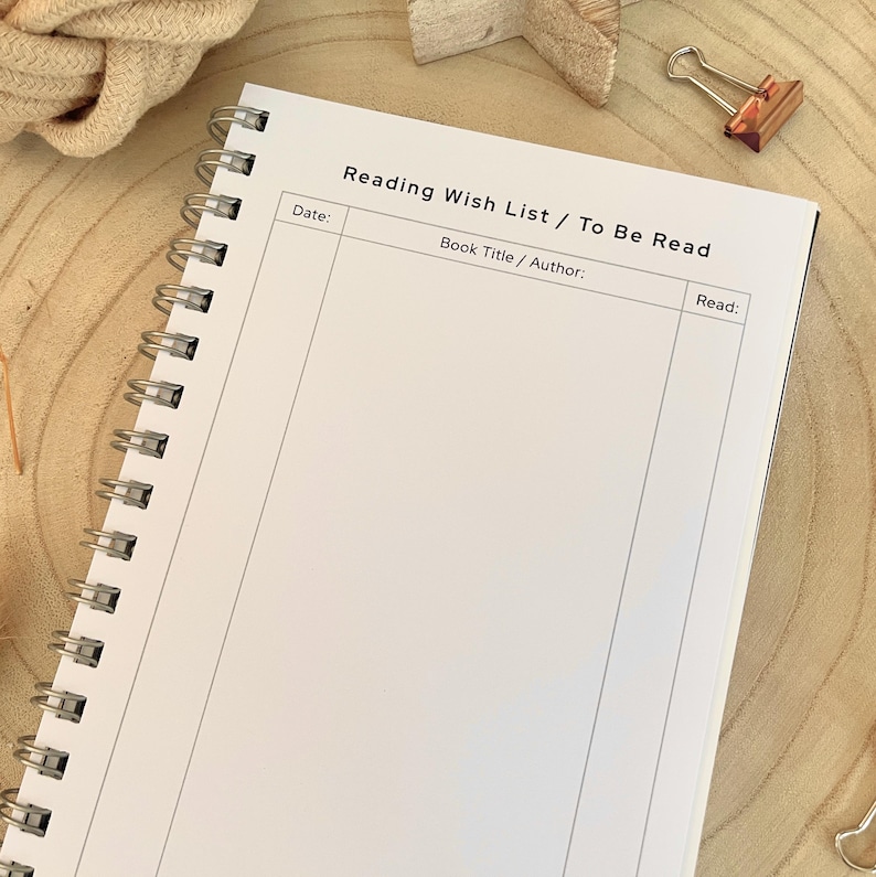 Puede incluir: Un cuaderno en espiral blanco con el texto "Reading Wish List / To Be Read". El cuaderno tiene secciones para la fecha, el t&iacute;tulo/autor del libro y una secci&oacute;n de lectura. El cuaderno est&aacute; abierto sobre una superficie de madera.