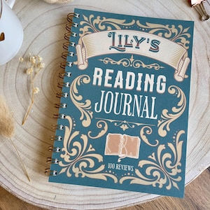 Puede incluir: Un diario de lectura con espiral y cubierta color turquesa con el texto "Lily's Reading Journal" en letras blancas y doradas. La cubierta tiene adornos decorativos y una ilustraci&oacute;n de libro. Dise&ntilde;ado para 100 rese&ntilde;as.