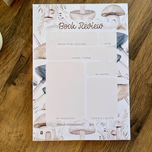 Könnte beinhalten: Eine druckbare Buchrezensionsvorlage mit einem Pilz-Thema. Die Vorlage enthält Abschnitte für Buchtitel, Autor, Datum, Genre, Bewertung, Gedanken und eine Kritzelei oder ein Zitat. Der Hintergrund ist eine Aquarellillustration von Pilzen und Blättern.