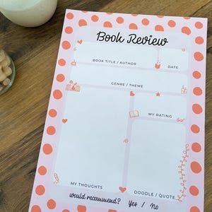May include: A pink book review notepad with a polka dot border and the words "Book Review" at the top. The notepad includes sections for book title, author, date, genre, thoughts, rating, and a doodle/quote area. It also asks "Would recommend? Yes / No."