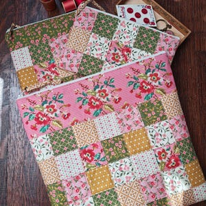 May include: Two quilted zipper pouches with patchwork patterns. The pouches feature a mix of floral and geometric fabrics in pink, green, and gold. One pouch has a pink floral design, and the other has a patchwork design.