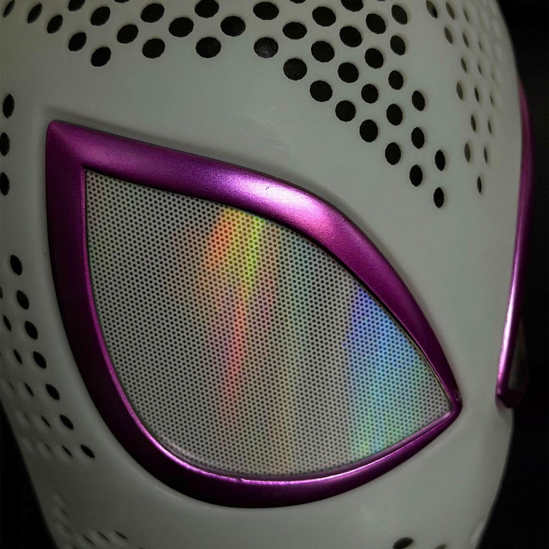 May include: A white mask with a purple outline around the eye openings. The eye openings have a mesh screen with a rainbow holographic effect. The mask has small black circular cutouts across the surface.