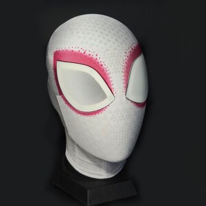 Puede incluir: Una m&aacute;scara blanca de Spider-Gwen con detalles rosas alrededor de los ojos. La m&aacute;scara tiene una superficie texturizada con peque&ntilde;os puntos espaciados uniformemente. Las aberturas de los ojos son blancas con un patr&oacute;n de malla.