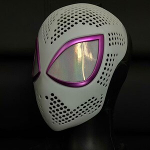 May include: White mask with a perforated pattern and purple eye surrounds. The eye openings feature a mesh material. The mask is likely for cosplay or costume use.