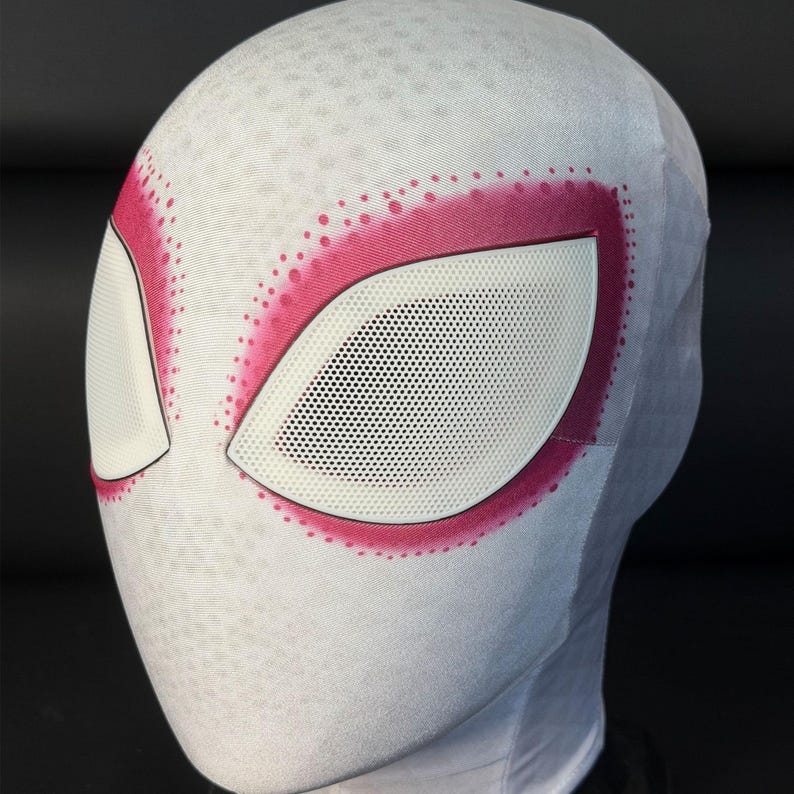 Puede incluir: Una m&aacute;scara blanca de Spider-Gwen con detalles rosas alrededor de los ojos. Las aberturas de los ojos son blancas con un patr&oacute;n de malla negra. La m&aacute;scara tiene una superficie texturizada y est&aacute; dise&ntilde;ada para la cabeza.