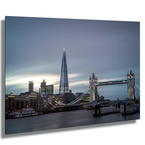 Puede incluir: Fotografía del horizonte de Londres al anochecer. La imagen presenta el rascacielos The Shard, el Tower Bridge y otros edificios a lo largo del río Támesis. El cielo es azul y gris.