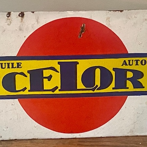 Puede incluir: Un letrero metálico rectangular con fondo blanco, un círculo rojo grande y un rectángulo horizontal amarillo que contiene el texto azul oscuro HUILE CELOR AUTOS. El letrero presenta manchas de óxido visibles y pequeños agujeros en los bordes.