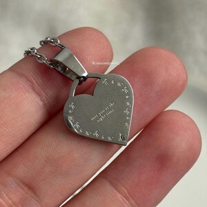 May include: Silver heart-shaped pendant necklace with a chain. The pendant has a small diamond-shaped stone and the inscription "met you at the right time".