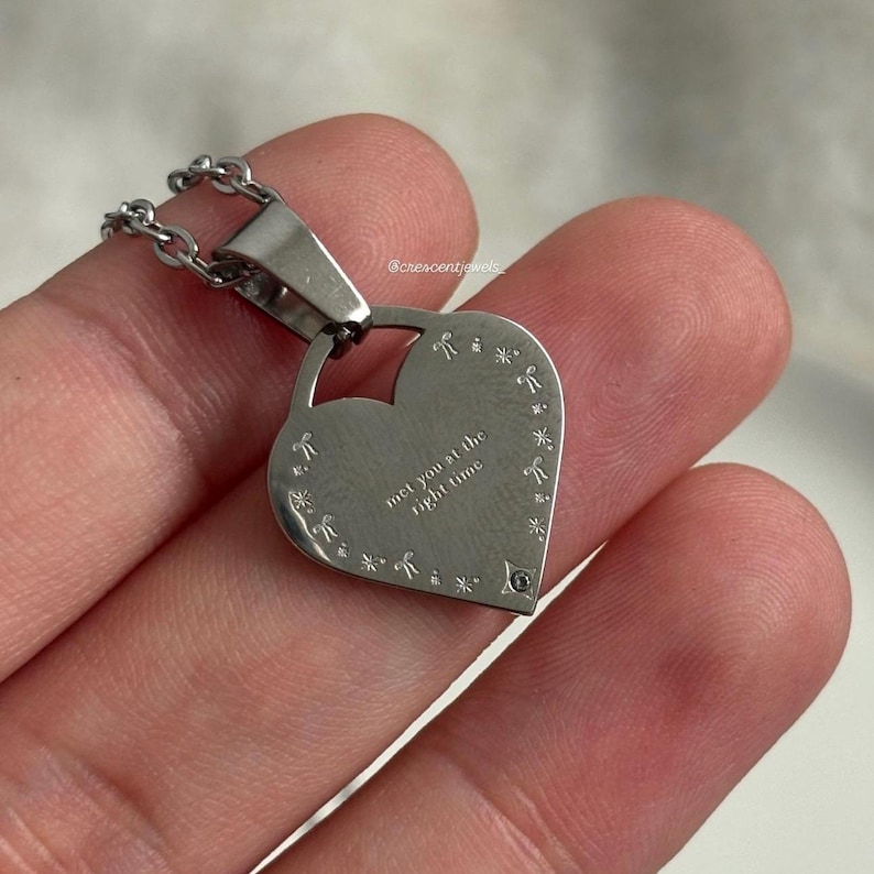 May include: Silver heart-shaped pendant necklace with a chain. The pendant has a small diamond-shaped stone and the inscription "met you at the right time".