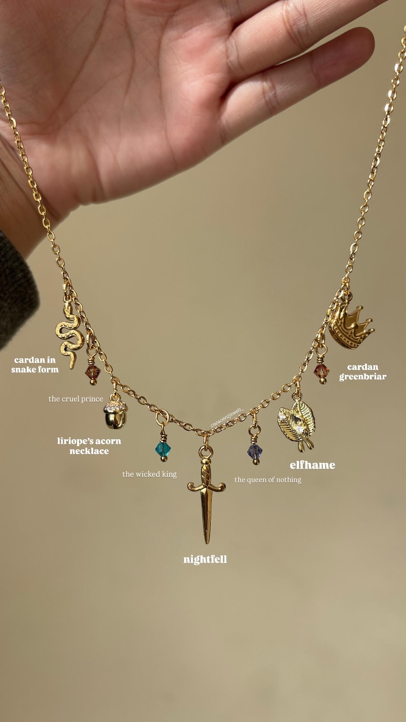 May include: A gold-coloured necklace featuring various charms: a snake, crown, acorn, leaf, and sword, embellished with colourful beads. The image includes text such as "cardan in snake form", "the cruel prince", "liriope's acorn necklace", "elfhame", "the wicked king", "the queen of nothing", "nightfell", and "cardan greenbriar".
