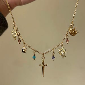 May include: Gold necklace with charms: a snake, crown, acorn, leaf, and dagger. It also has small, colourful crystal beads. A delicate piece of jewellery.