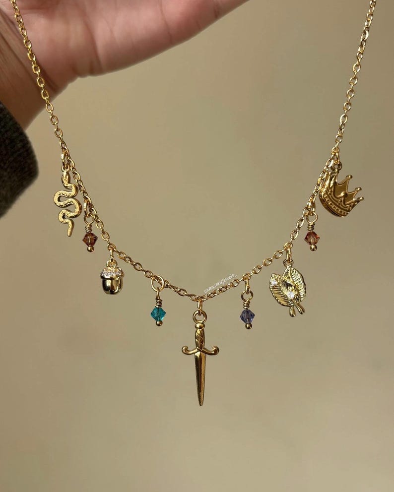 May include: Gold necklace with charms: a snake, crown, acorn, leaf, and dagger. It also has small, colourful crystal beads. A delicate piece of jewellery.