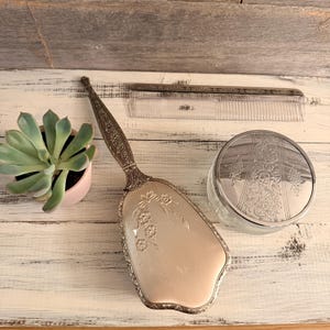 Conjunto de toucador vintage selecionado, banhado a prata, composto por escova, pente e frasco de vidro com tampa.
