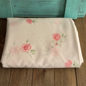 Puede incluir: Tela blanca con un delicado estampado floral rosa. La tela presenta pequeñas rosas rosas con hojas verdes dispersas por la superficie.