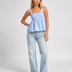 May include: A light blue sleeveless peplum top with wide shoulder straps and a square neckline, paired with light-wash blue denim jeans that feature a straight-leg cut and a classic five-pocket design, worn with simple brown leather slide sandals.