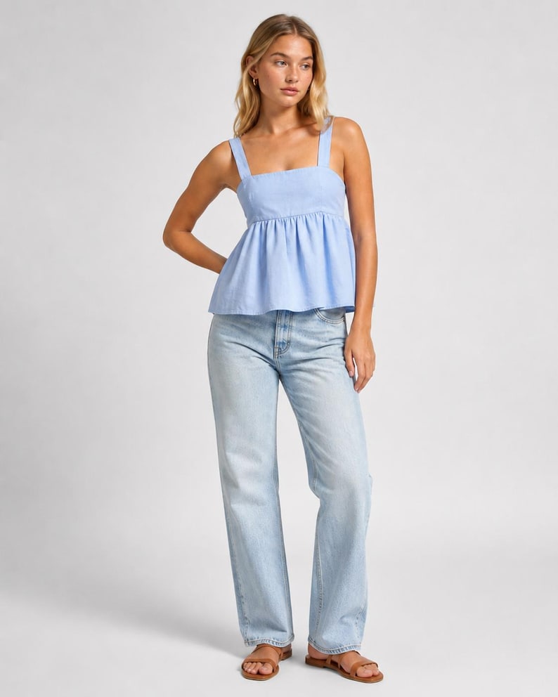 May include: A light blue sleeveless peplum top with wide shoulder straps and a square neckline, paired with light-wash blue denim jeans that feature a straight-leg cut and a classic five-pocket design, worn with simple brown leather slide sandals.