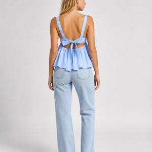 May include: A light blue sleeveless peplum top featuring wide shoulder straps and a tie-back closure, paired with light-wash blue denim jeans. The top has a gathered waistline and an open back design, while the jeans are full-length.