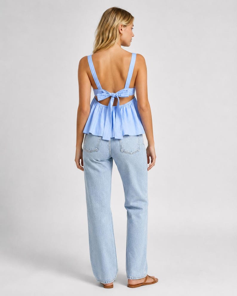 May include: A light blue sleeveless peplum top featuring wide shoulder straps and a tie-back closure, paired with light-wash blue denim jeans. The top has a gathered waistline and an open back design, while the jeans are full-length.