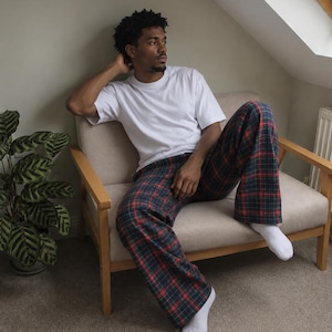 May include: A plain white short-sleeved t-shirt paired with loose-fitting trousers featuring a dark green, navy blue, and red plaid tartan pattern. The outfit is completed with simple white socks, creating a relaxed and comfortable loungewear look.