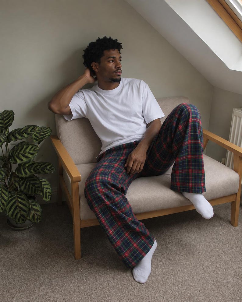 May include: A plain white short-sleeved t-shirt paired with loose-fitting trousers featuring a dark green, navy blue, and red plaid tartan pattern. The outfit is completed with simple white socks, creating a relaxed and comfortable loungewear look.