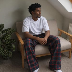 May include: A plain white short-sleeved crew neck t-shirt paired with loose-fitting lounge pants featuring a dark green, navy blue, and red plaid tartan pattern. The outfit is completed with simple white socks worn on the feet.