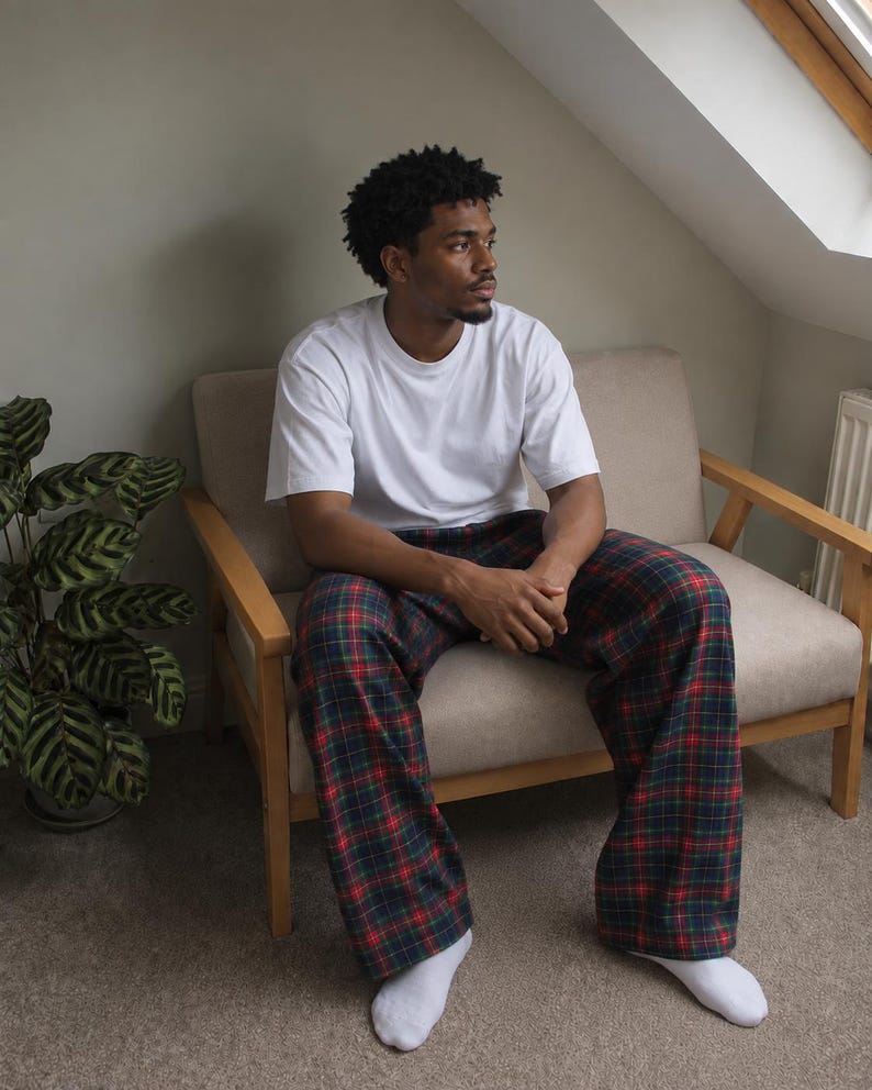 May include: A plain white short-sleeved crew neck t-shirt paired with loose-fitting lounge pants featuring a dark green, navy blue, and red plaid tartan pattern. The outfit is completed with simple white socks worn on the feet.