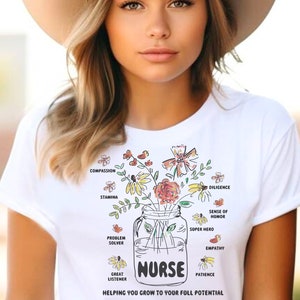 May include: White t-shirt with a floral design in a mason jar and the word "NURSE" in black. The shirt includes the text "HELPING YOU GROW TO YOUR FULL POTENTIAL" and other words like "compassion" and "patience".