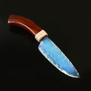 Puede incluir: Un cuchillo artesanal con mango de madera marrón oscuro y una hoja translúcida azul claro. El mango está envuelto con un cordón color crema cerca de la hoja.