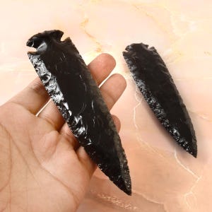 May include: Two black obsidian arrowheads with a pointed tip and a textured surface.