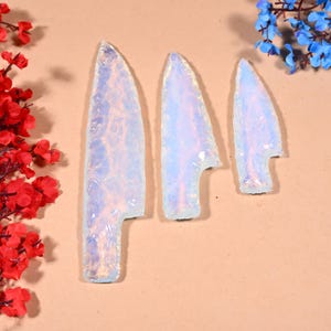 May include: Three iridescent white opal arrowheads of varying sizes. The arrowheads are smooth and have a translucent, milky white appearance.
