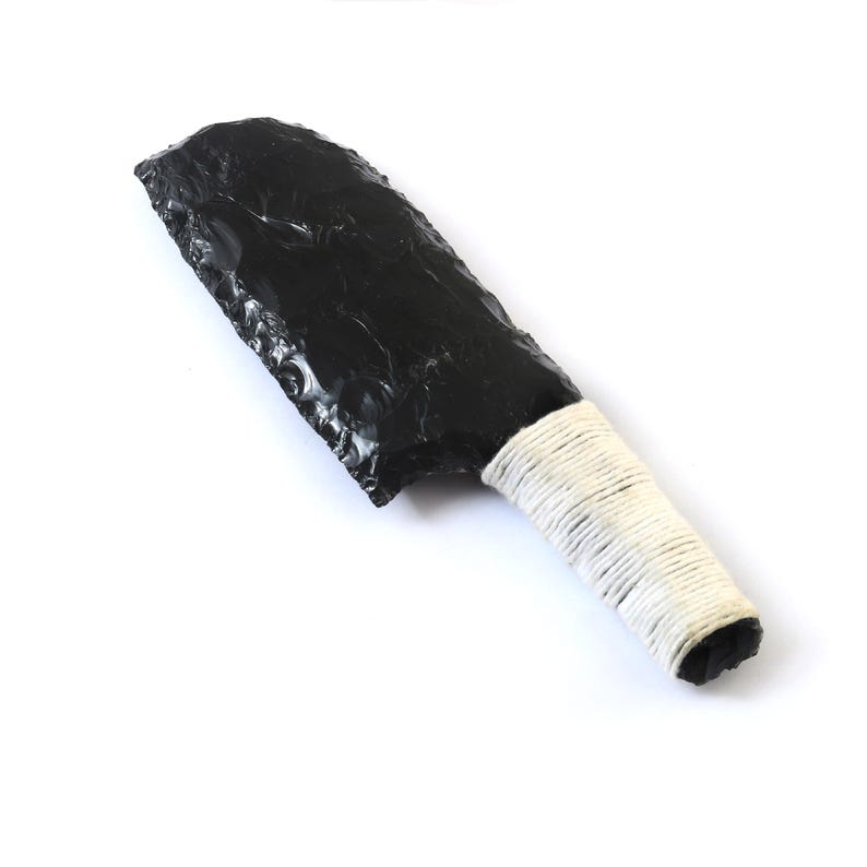 May include: A black obsidian knife with a white wrapped handle. The blade is a dark, glossy black with a rough, chipped edge. The handle is tightly wrapped with white cord.