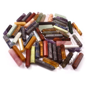 May include: A collection of colorful, polished, pointed crystal wands. The wands are made of various types of gemstones, including amethyst, rose quartz, tiger's eye, and clear quartz.