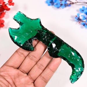 May include: A green glass axe head, also known as a hand axe, is a decorative piece of art. The axe head is made of green glass and has a sharp edge.
