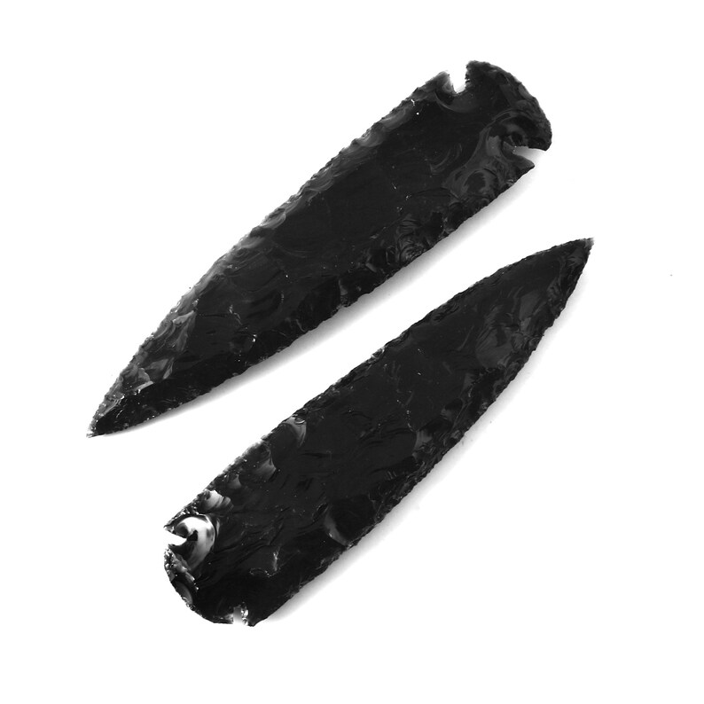 May include: Two black obsidian arrowheads, also known as spear points, with a sharp point and a slightly curved base.