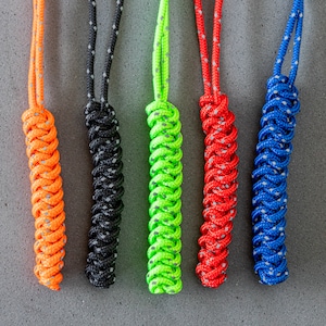 May include: Six colorful braided keychains with white accents. The keychains are orange, black, green, red, and blue.